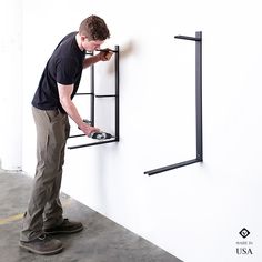 a man is working on a wall mounted shelf with two black brackets and one has his hands in the drawer