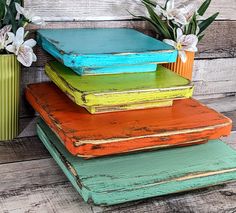 four different colored wooden trays stacked on top of each other with flowers in the background