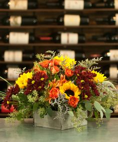 a vase filled with lots of flowers sitting on top of a table next to bottles of wine