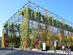 people are walking in front of a building covered with plants