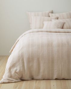 an unmade bed with beige linens in a white walled room and wood flooring