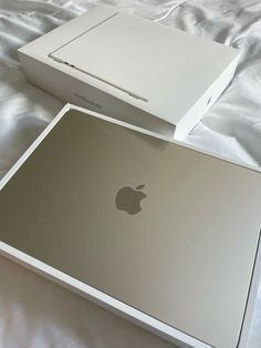 two apple laptops sitting side by side on a white bed with the box open