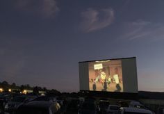 an outdoor movie screen in the middle of a parking lot with cars parked around it