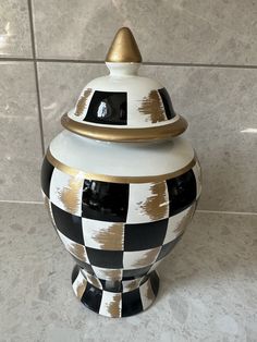 a black and white checkerboard jar with gold trim on the lid sitting on a tile floor