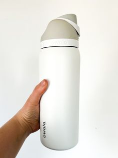 a hand holding a white and black water bottle with the lid up against a white background