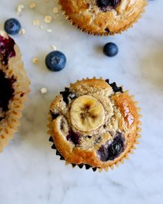 three blueberry muffins with a banana cut in half on a marble surface