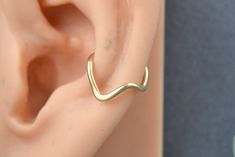 an ear is shown with a gold colored nose ring on top of the ear, which has a curved design