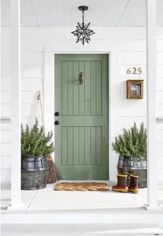 a green front door on a white house with two buckets full of potted plants