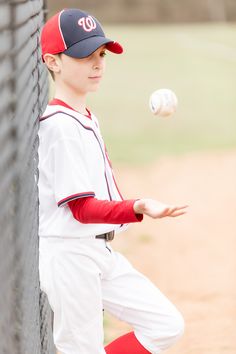 a young baseball player leaning against the wall with his glove and ball in mid air