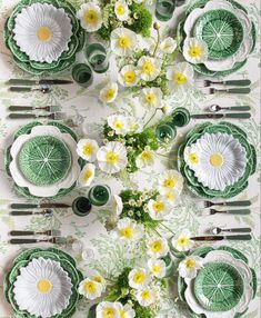 the table is set with green and white plates, silverware, and flower arrangements