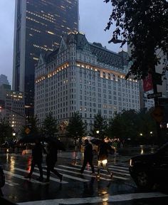 people crossing the street at night in front of a large building with lights on it