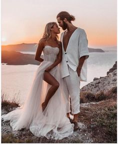 a man and woman standing next to each other on top of a hill near the ocean