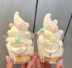 two people holding up small cups with ice cream and marshmallows on them