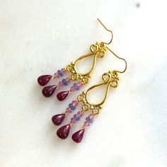 Polished rich rubies are stunning in their clarity and rich hue. The plump teardrops sway from beneath gorgeous highly detailed 22kg vermeil earrings studded with tanzanite and pink sapphires. The length is a perfectly wearable but dramatic 2.5 inches long. This is a one and only pair of fine gemstone jewels - please inquire about the matching necklace. Gold Teardrop Earrings With Gemstone Accents, Elegant Garnet Briolette Earrings, Elegant Briolette Garnet Earrings, Gold Ruby Chandelier Earrings As Gift, Gold Garnet Teardrop Earrings, Gold Teardrop Garnet Earrings, Yellow Gold Teardrop Ruby Earrings, Gold Ruby Teardrop Jewelry, Gold Ruby Gemstone Earrings