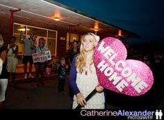 a woman holding a heart shaped sign in front of a building