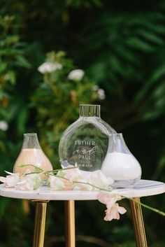 two vases sitting on top of a white table next to flowers and greenery