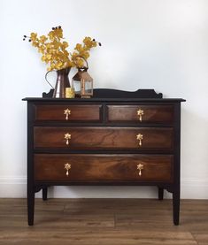 a wooden dresser with flowers on top and a vase in the corner next to it