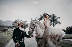 a man and woman in mexican garb standing next to a white horse