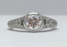 a white gold ring with an oval cut diamond surrounded by filigrees and diamonds