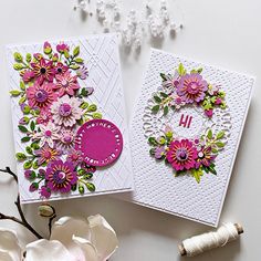 two cards with flowers on them sitting next to some spools of thread and beads