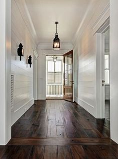 an empty hallway with wood flooring and white walls, along with two lanterns hanging from the ceiling