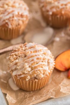 a muffin with white icing sitting on top of a piece of paper next to sliced peaches