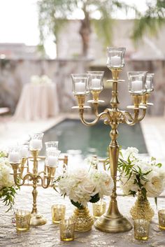 a gold candelabra with white flowers and candles on it next to a pool