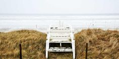 a white chair sitting on top of a grass covered field next to the ocean and beach