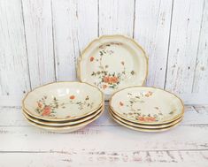 four plates with flowers on them are stacked up against a white wooden wall and one has an orange flower in the center