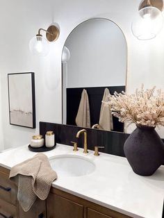 a bathroom sink with a large mirror above it and flowers in a vase on the counter