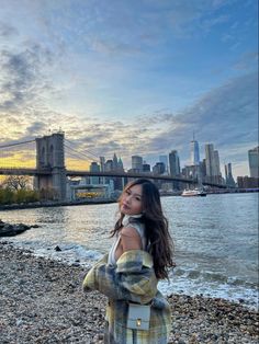 a woman standing on top of a rocky beach next to the water with a city skyline in the background