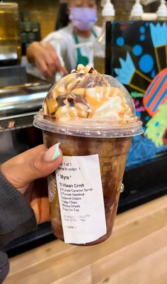 a person holding up a plastic cup filled with ice cream and caramel toppings