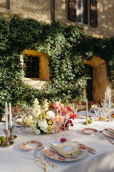 the table is set with plates and silverware on it, along with an ivy covered wall