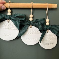 three ceramic ornaments hanging from a wooden stick with green ribbons and bows on the top