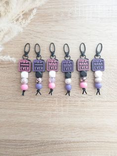 six keychains with different colored beads and words on them, all hanging from black metal hooks