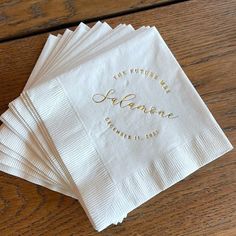 six personalized napkins with gold foil lettering on them sitting on a wooden table