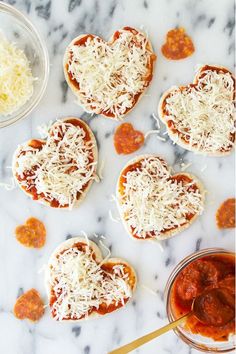 small heart shaped pizzas with cheese and sauce on a marble counter top, ready to be eaten