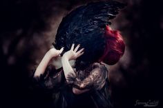 a woman with red hair and black feathers on her head is holding a large bird