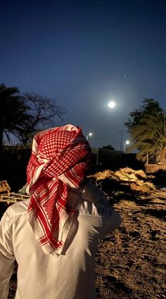 a man wearing a red and white checkered scarf standing in front of the moon