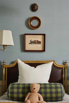 a teddy bear sitting on top of a bed next to a lamp and framed pictures