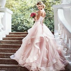 a woman in a pink dress is standing on some steps and holding a flower bouquet