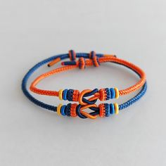 an orange and blue rope bracelet with two small beads on it's end, sitting on top of a white surface