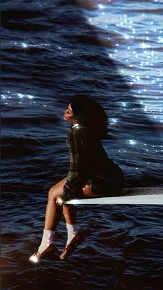 a woman sitting on top of a surfboard in the middle of the ocean at night