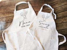 two personalized aprons are sitting on a wooden table, one is white and the other has black writing