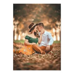 a man and woman sitting on the ground in front of trees with leaves around them