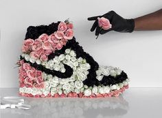 a shoe made out of flowers is being held by someone's hand with a pair of gloves on it