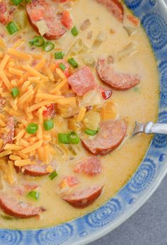 a blue and white bowl filled with soup topped with ham, cheese and green onions