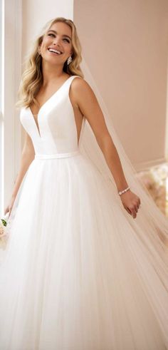 a woman in a white wedding dress standing next to a window and smiling at the camera