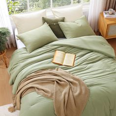 a bed with green sheets and pillows in front of a window next to a plant