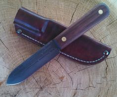 a knife sitting on top of a piece of wood next to a leather sheath with holes in it